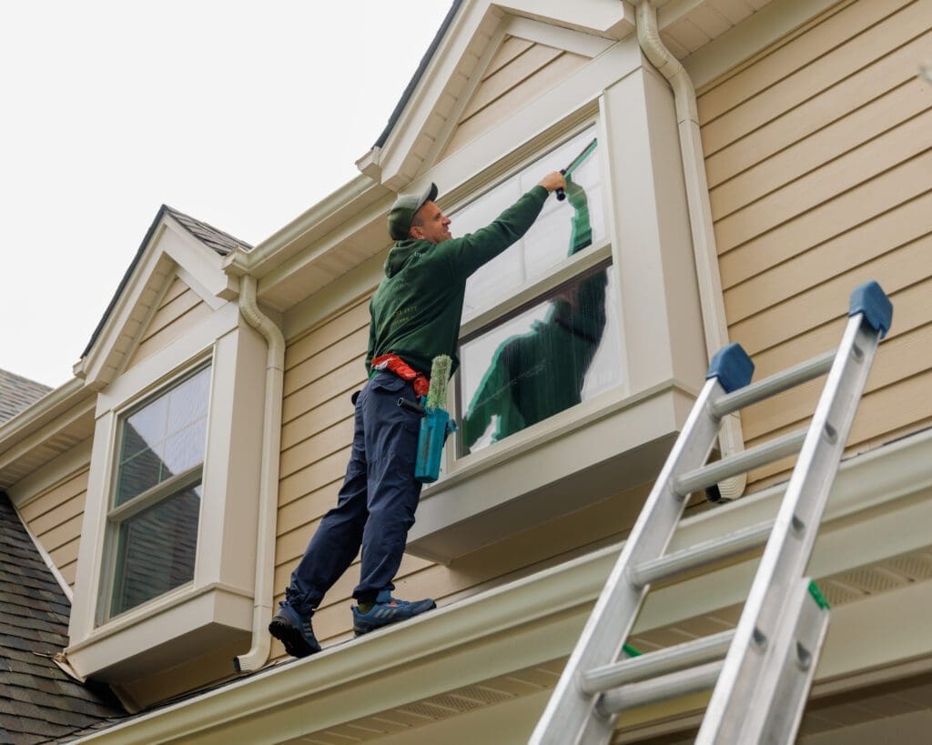 man cleaning a second story window cleaning with a squeegee