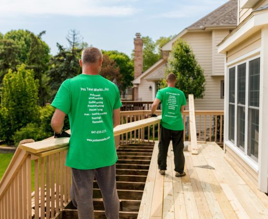 Two men carrying lumber for deck installation.